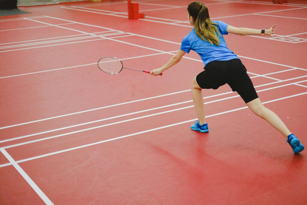 Back view of a woman playing badminton on an indoor court. Action shot capturing skill and movement.